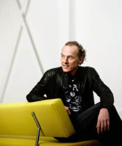 Richard Hutten sat on a mustard colour sofa. Design Mumbai.